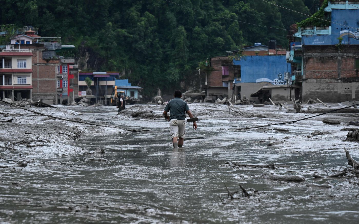 A resident navigates a mud-covered street after flash floods and a landslide in Devighat. Photo credit: PRAKASH MATHEMA